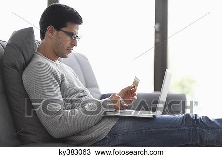 Man holding a credit card and using a laptop View Large Photo Image Stock Image - Man holding a credit card and using a laptop. Fotosearch