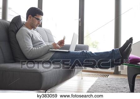 Stock Photo - Man holding a credit card and using a laptop. Fotosearch