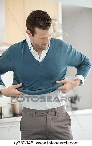 Stock Photograph - Man putting on sweater in the kitchen. Fotosearch