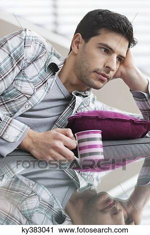 Stock Image - Man reclining on a couch and drinking coffee. Fotosearch