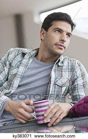 Stock Image - Man reclining on a couch and drinking coffee. Fotosearch