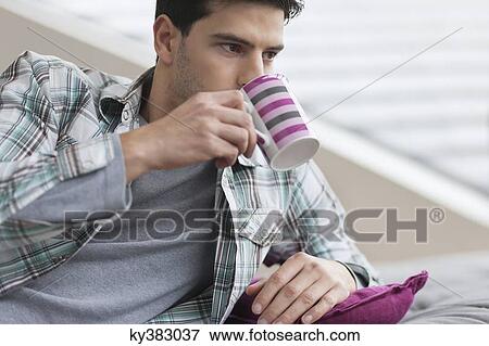 Stock Photo - Man reclining on a couch and drinking coffee. Fotosearch