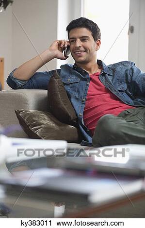 Man reclining on a couch and talking on a mobile phone View Large Photo Image Stock Image - Man reclining on a couch and talking on a mobile phone. Fotosearch