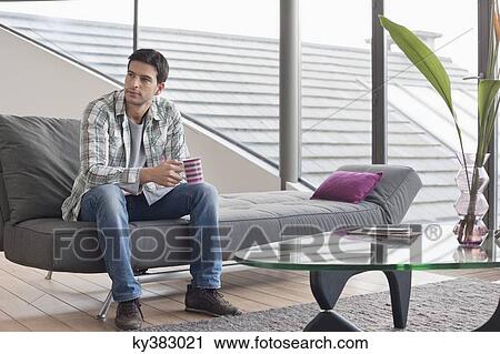 Man sitting on a couch and drinking coffee View Large Photo Image Stock Image - Man sitting on a couch and drinking coffee. Fotosearch