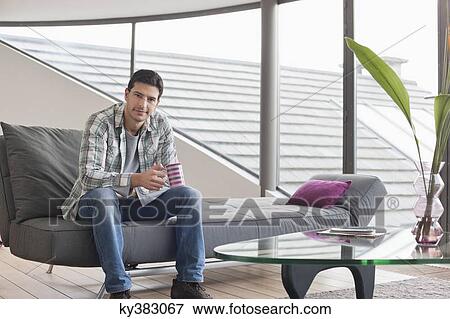 Man sitting on a couch and drinking coffee View Large Photo Image Stock Photo - Man sitting on a couch and drinking coffee. Fotosearch