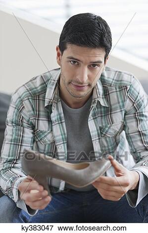 Man sitting on a couch and holding a high heel shoe View Large Photo Image Stock Photo - Man sitting on a couch and holding a high heel shoe. Fotosearch