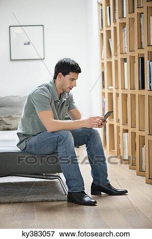 Man sitting on a couch and reading an electronic book View Large Photo Image Stock Photo - Man sitting on a couch and reading an electronic book. Fotosearch