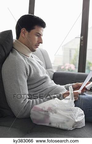 Man sitting on a couch reading medical prescription View Large Photo Image Stock Photograph - Man sitting on a couch reading medical prescription. Fotosearch