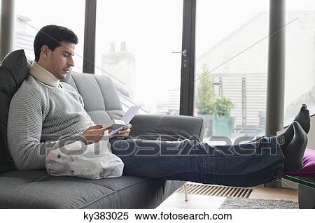 Man sitting on a couch reading medical prescription View Large Photo Image Stock Photography - Man sitting on a couch reading medical prescription. Fotosearch