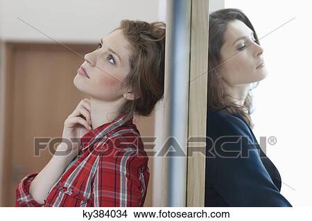 Two female friends standing back to back against a door View Large Photo Image Picture - Two female friends standing back to back against a door. Fotosearch