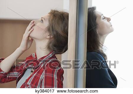 Two female friends standing back to back against a door View Large Photo Image Stock Photo - Two female friends standing back to back against a door. Fotosearch