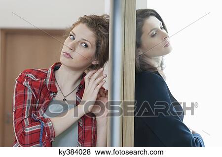 Two female friends standing back to back against a door View Large Photo Image Stock Photo - Two female friends standing back to back against a door. Fotosearch