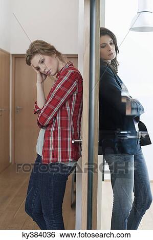 Two female friends standing back to back against a door View Large Photo Image Stock Photograph - Two female friends standing back to back against a door. Fotosearch