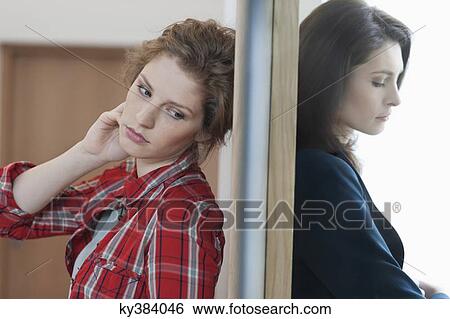 Two female friends standing back to back against a door View Large Photo Image Stock Photograph - Two female friends standing back to back against a door. Fotosearch