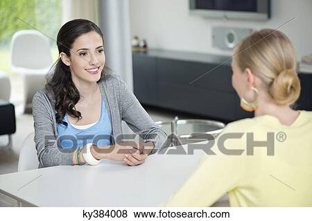 Two woman sitting at the table across each other View Large Photo Image Stock Photo - Two woman sitting at the table across each other. Fotosearch