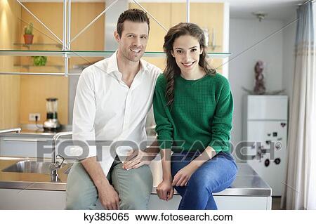 Stock Photography - Couple sitting on the kitchen counter and smiling. Fotosearch