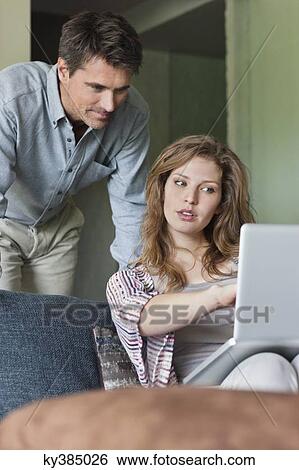 Couple using a laptop at home View Large Photo Image Stock Photograph - Couple using a laptop at home. Fotosearch