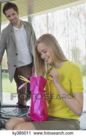 Stock Image - Happy woman opening a present given by her boyfriend. Fotosearch