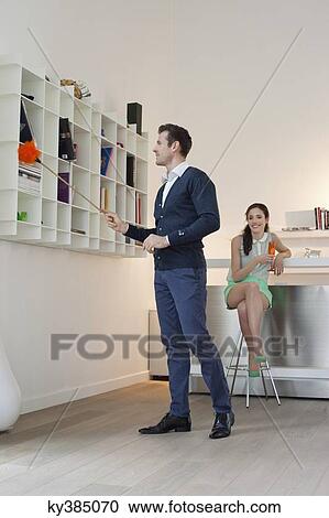 Man cleaning a bookshelf with his wife drinking champagne in the background View Large Photo Image Stock Image - Man cleaning a bookshelf with his wife drinking champagne in the background. Fotosearch