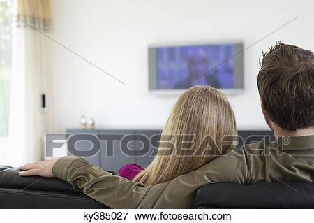 Rear view of a couple watching television View Large Photo Image Stock Photo - Rear view of a couple watching television. Fotosearch