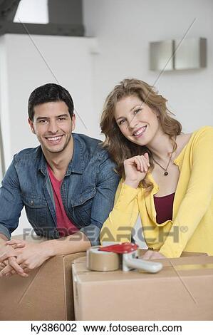 Couple leaning over cardboard boxes and smiling View Large Photo Image Stock Image - Couple leaning over cardboard boxes and smiling. Fotosearch