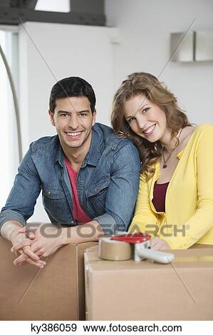 Couple leaning over cardboard boxes and smiling View Large Photo Image Stock Photo - Couple leaning over cardboard boxes and smiling. Fotosearch