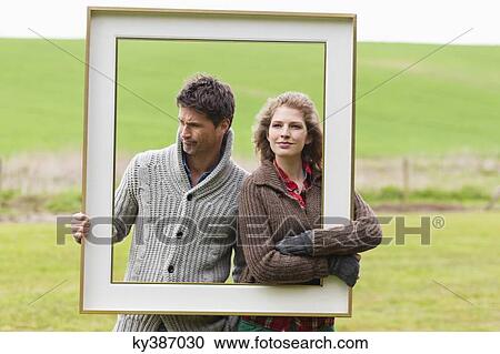 Stock Image - Couple holding a frame in a field. Fotosearch