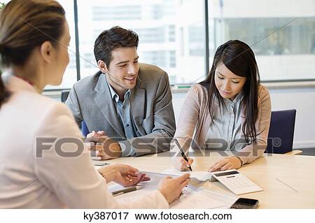 Stock Photo - Couple signing documents with real estate agent. Fotosearch