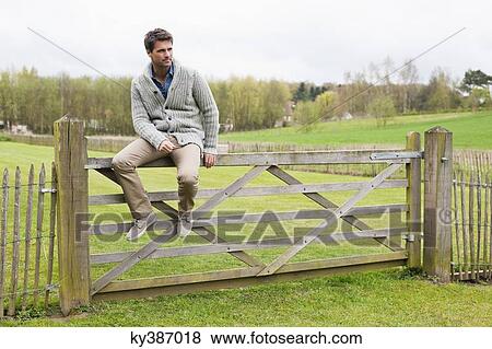 Man sitting on the gate of a cottage View Large Photo Image Stock Photo - Man sitting on the gate of a cottage. Fotosearch