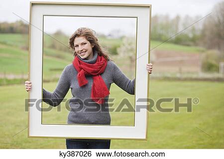 Portrait of a woman standing with a frame in a park View Large Photo Image Stock Photograph - Portrait of a woman standing with a frame in a park. Fotosearch
