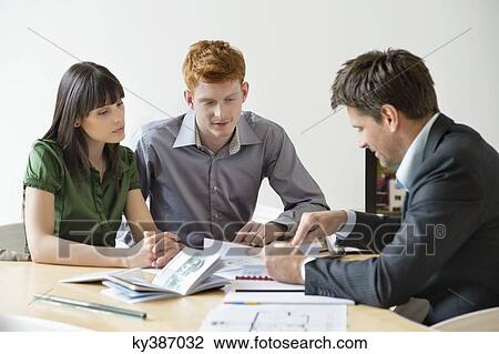 Stock Image - Real estate agent discussing property documents to his clients. Fotosearch
