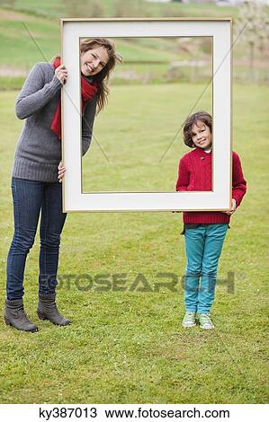 Stock Image - Woman and her son standing with a frame in a park. Fotosearch