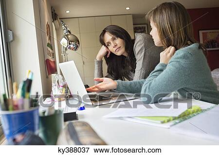 Stock Photo - Girl studying with her mother on a laptop at home. Fotosearch