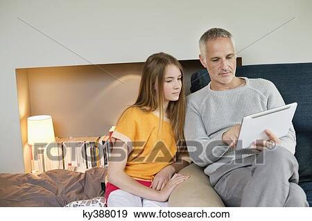 Stock Photo - Man using a digital tablet with his daughter at home. Fotosearch