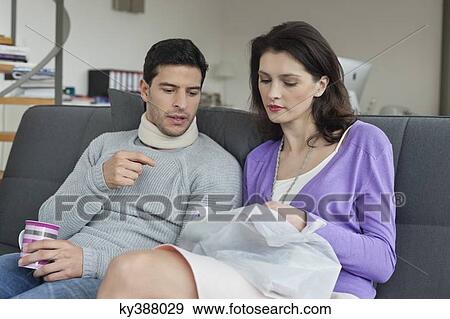 Stock Photo - Woman giving medicine to her husband suffering from neckache. Fotosearch