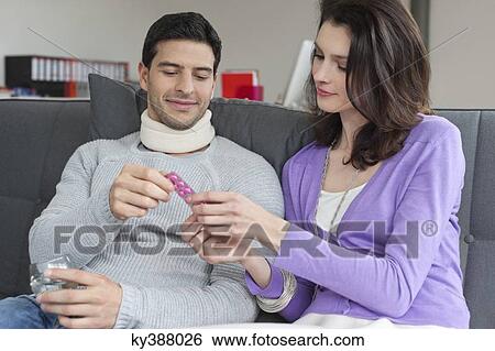 Woman giving medicine to her husband suffering from neckache View Large Photo Image Stock Photograph - Woman giving medicine to her husband suffering from neckache. Fotosearch