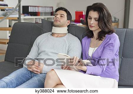 Picture - Woman reading a book for her husband suffering from neckache. Fotosearch