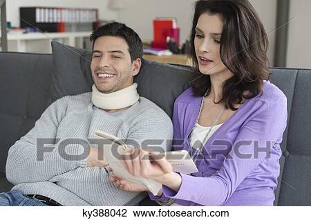 Woman reading a book for her husband suffering from neckache View Large Photo Image Stock Image - Woman reading a book for her husband suffering from neckache. Fotosearch