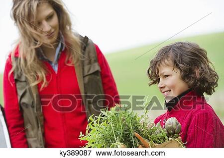 Boy holding a crate of assorted vegetables with his mother in a farm View Large Photo Image Stock Photo - Boy holding a crate of assorted vegetables with his mother in a farm. Fotosearch