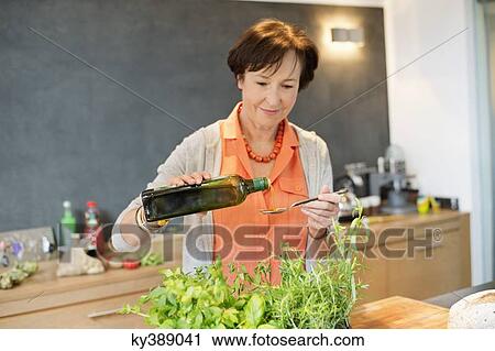 Stock Image - Elderly woman pouring olive oil into a spoon. Fotosearch