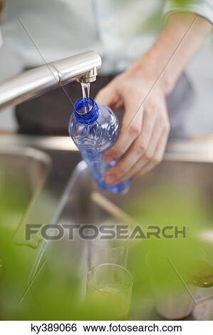 Man filling a bottle with water in the kitchen View Large Photo Image Stock Photograph - Man filling a bottle with water in the kitchen. Fotosearch