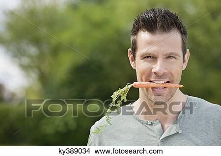 Picture - Man holding a carrot in his mouth. Fotosearch