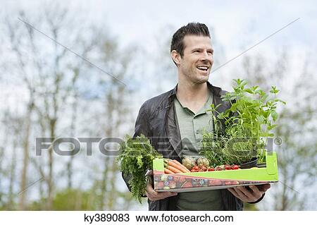 Stock Image - Man holding a tray of raw vegetables. Fotosearch
