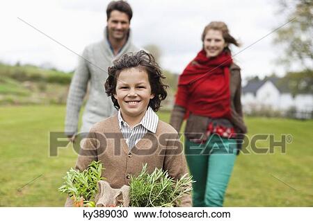 Stock Image - Portrait of a boy holding a basket of vegetables with his parents in a farm. Fotosearch