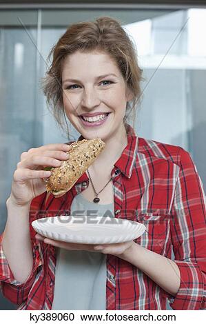Stock Image - Portrait of a woman eating sandwich and smiling. Fotosearch