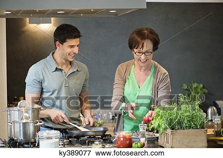 Woman assisting her son to cook food in the kitchen View Large Photo Image Stock Photo - Woman assisting her son to cook food in the kitchen. Fotosearch