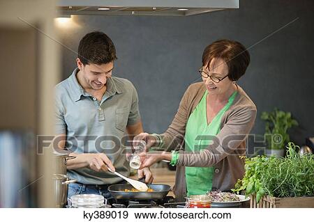 Woman assisting her son to cook food View Large Photo Image Stock Photo - Woman assisting her son to cook food. Fotosearch