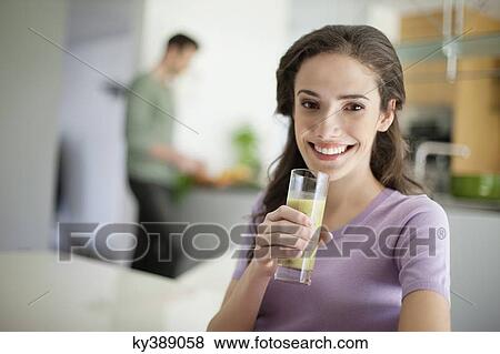 Woman drinking soup with her husband preparing food in the background View Large Photo Image Stock Photo - Woman drinking soup with her husband preparing food in the background. Fotosearch