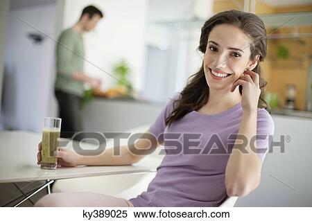 Stock Photography - Woman drinking soup with her husband preparing food in the background. Fotosearch