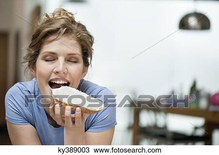 Stock Image - Woman eating toast with cream spread on it. Fotosearch